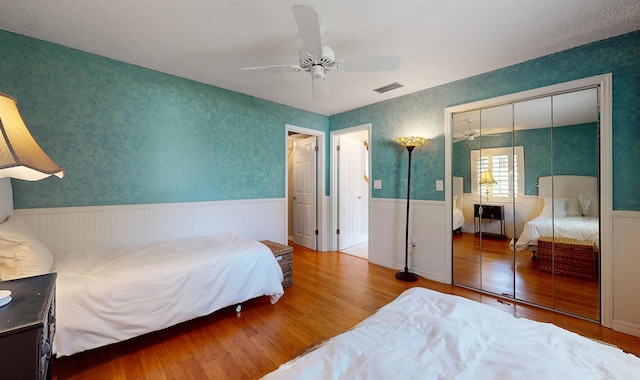 bedroom featuring a ceiling fan, a wainscoted wall, visible vents, and wood finished floors