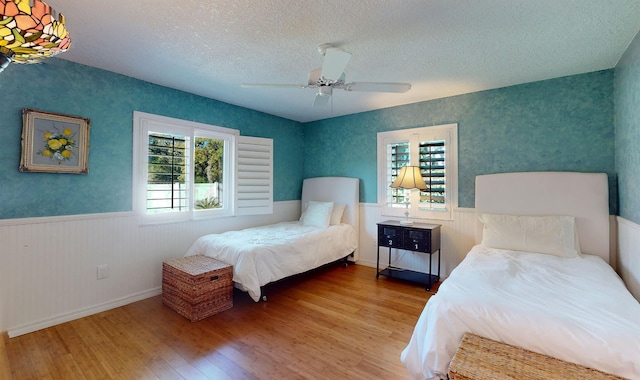 bedroom featuring wallpapered walls, a wainscoted wall, ceiling fan, hardwood / wood-style flooring, and a textured ceiling