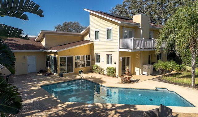 back of house with stucco siding, a patio area, an outdoor pool, and solar panels