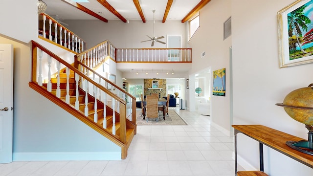 tiled entryway featuring baseboards, a ceiling fan, a high ceiling, stairs, and beam ceiling