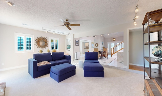 carpeted living area with visible vents, rail lighting, ceiling fan, a textured ceiling, and baseboards