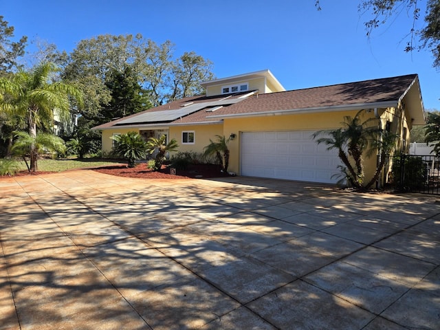 view of front of house featuring an attached garage, solar panels, fence, driveway, and stucco siding