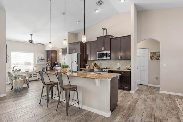 kitchen with arched walkways, a breakfast bar area, stainless steel appliances, visible vents, and dark brown cabinets