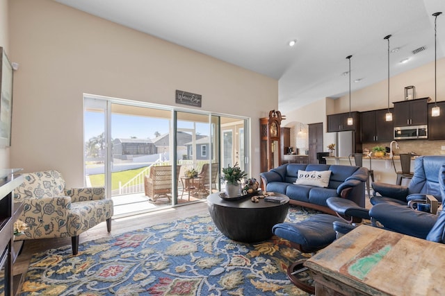 living area with high vaulted ceiling, visible vents, and wood finished floors