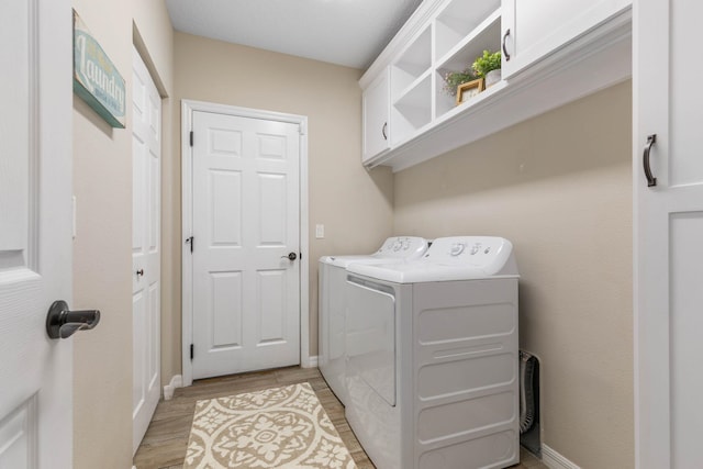 clothes washing area featuring cabinet space, light wood-style flooring, baseboards, and washer and dryer