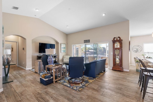 living area with arched walkways, lofted ceiling, visible vents, wood finished floors, and baseboards