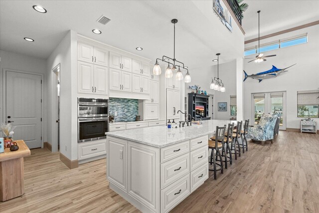 3 Menorca Way, Palm Coast, FL 32137 - kitchen with double oven, a ceiling fan, white cabinets, a kitchen bar, and light stone countertops