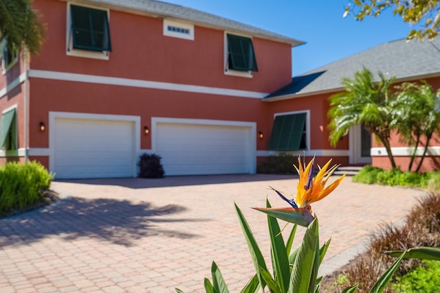 traditional-style home with decorative driveway, an attached garage, and stucco siding