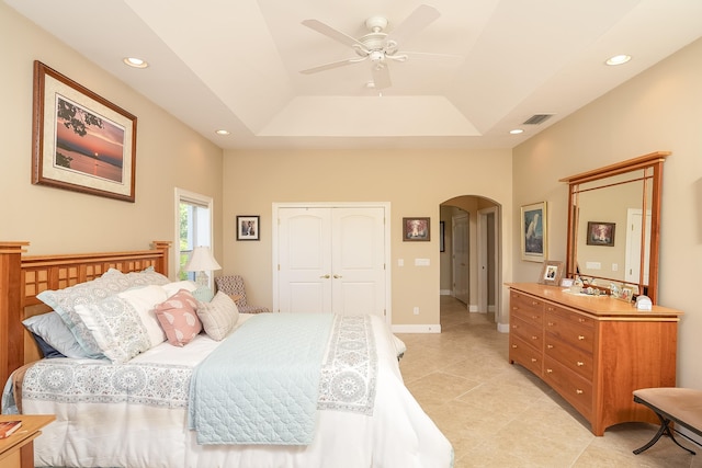 bedroom featuring visible vents, arched walkways, a raised ceiling, a closet, and light tile patterned flooring