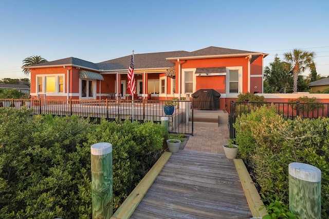 rear view of property featuring stucco siding, roof with shingles, and fence