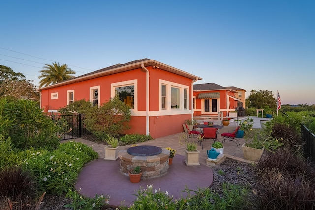rear view of property featuring fence, a patio, stucco siding, and a fire pit