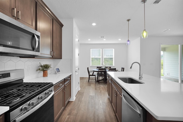 kitchen featuring hardwood / wood-style floors, sink, hanging light fixtures, an island with sink, and stainless steel appliances