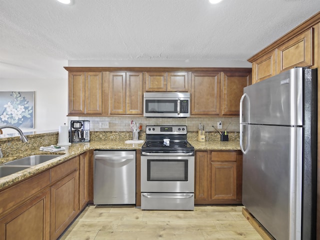 241 Tropic Way, Saint Augustine, FL 32080 - kitchen with stainless steel appliances, brown cabinets, light stone counters, light wood-style floors, and a textured ceiling