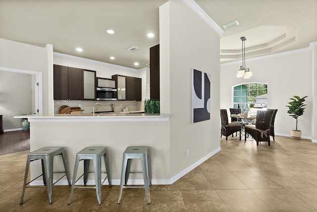 kitchen featuring pendant lighting, a breakfast bar, ornamental molding, dark brown cabinets, and kitchen peninsula