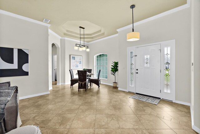 entryway with a tray ceiling, a wealth of natural light, and ornamental molding