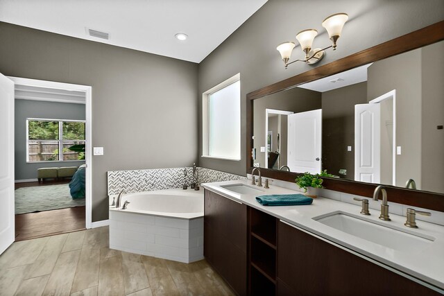 bathroom featuring wood-type flooring, vanity, a relaxing tiled tub, and a notable chandelier