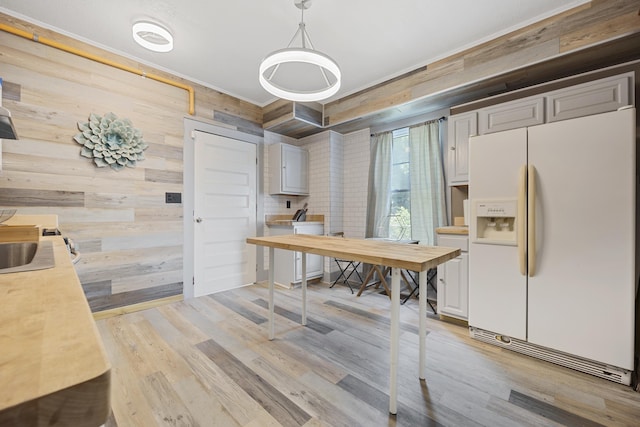 kitchen with pendant lighting, light wood-type flooring, white fridge with ice dispenser, and wooden walls