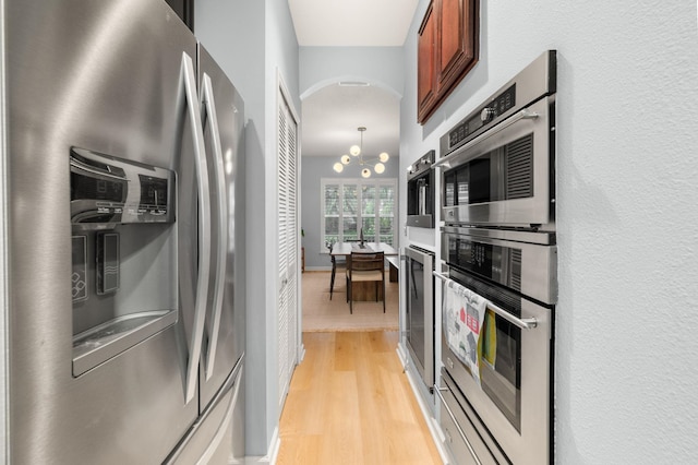 kitchen with arched walkways, a notable chandelier, light wood-style floors, appliances with stainless steel finishes, and brown cabinetry