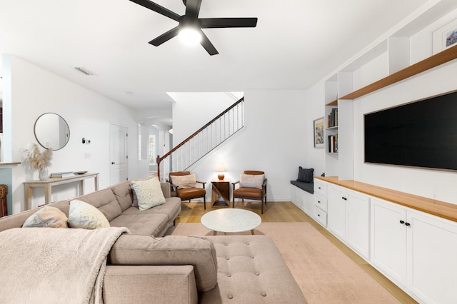 living room featuring light wood-type flooring, ceiling fan, and stairs