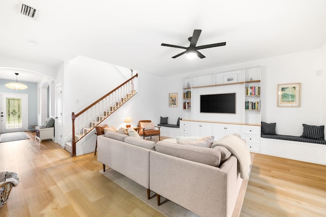 living room featuring arched walkways, visible vents, a ceiling fan, stairway, and light wood finished floors