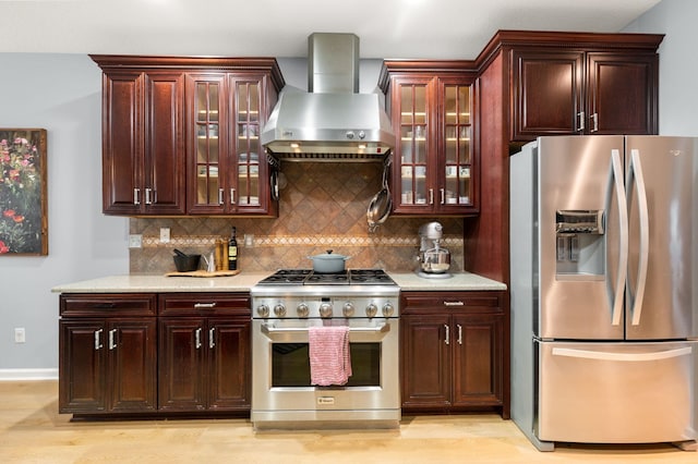 kitchen with light wood-style flooring, backsplash, appliances with stainless steel finishes, glass insert cabinets, and wall chimney exhaust hood