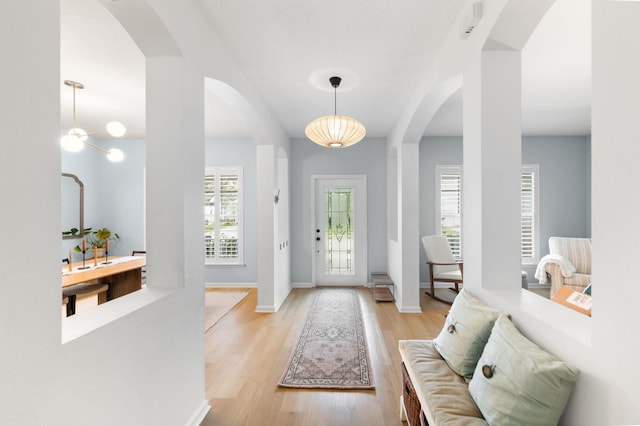 entryway with arched walkways, baseboards, and light wood finished floors