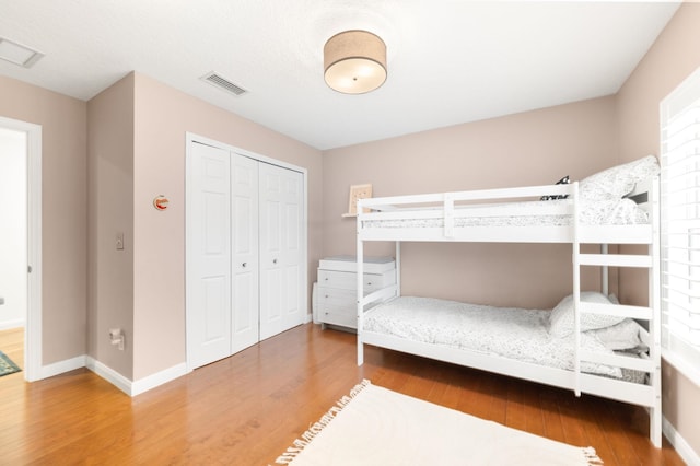 bedroom with baseboards, a closet, visible vents, and wood finished floors