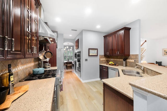 kitchen featuring visible vents, arched walkways, appliances with stainless steel finishes, wall chimney range hood, and a sink