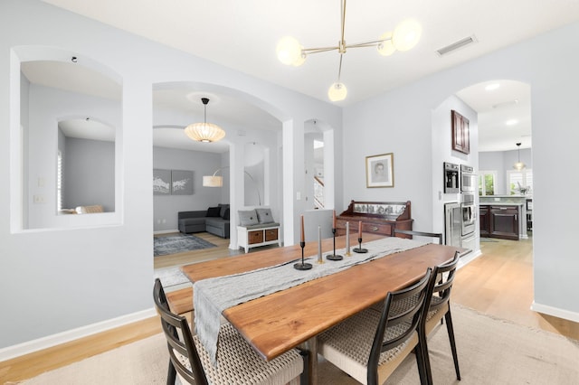 dining area with arched walkways, baseboards, visible vents, and light wood finished floors