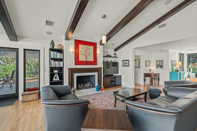 living area with visible vents, lofted ceiling with beams, light wood-style flooring, and a high end fireplace