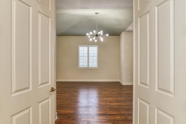 spare room with baseboards, dark wood-type flooring, an inviting chandelier, and vaulted ceiling