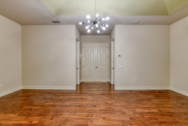 unfurnished room featuring an inviting chandelier, wood finished floors, visible vents, and baseboards