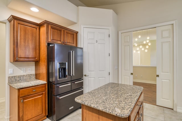 kitchen featuring light stone counters, a center island, brown cabinetry, and high end refrigerator