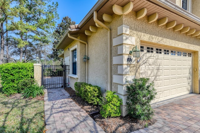 view of side of home with a gate, a garage, driveway, and stucco siding