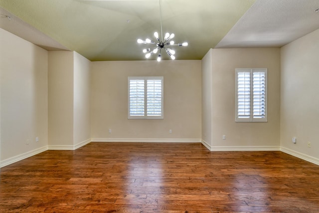 empty room featuring an inviting chandelier, wood finished floors, baseboards, and lofted ceiling