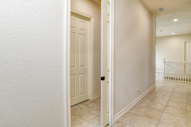 hallway with an upstairs landing, recessed lighting, light tile patterned flooring, baseboards, and a textured wall