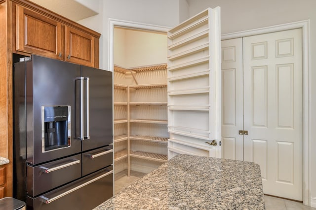 kitchen with light tile patterned floors, light stone countertops, high quality fridge, and brown cabinets