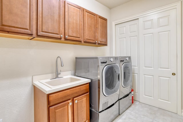 clothes washing area featuring a sink, cabinet space, light tile patterned flooring, and washer and clothes dryer