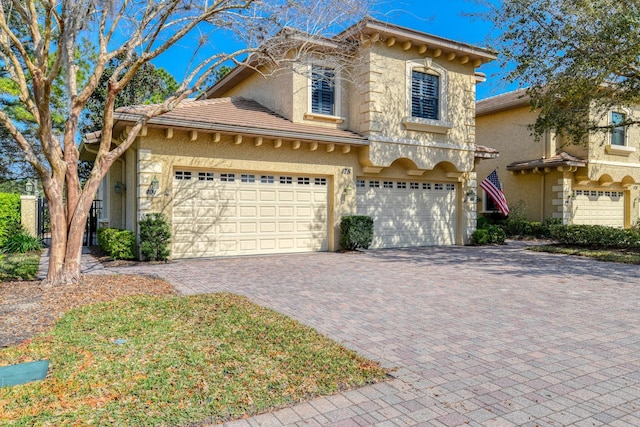 view of front of home with stucco siding, a tiled roof, decorative driveway, and a garage