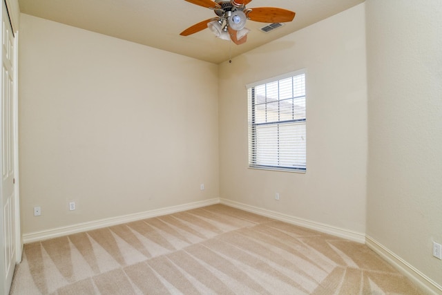 spare room featuring a ceiling fan, light colored carpet, visible vents, and baseboards