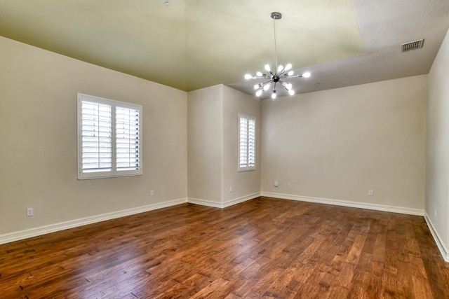 spare room featuring dark wood finished floors, baseboards, visible vents, and a chandelier