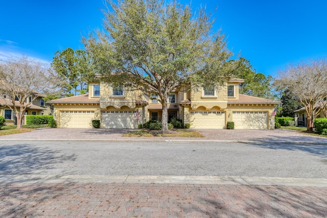 townhome / multi-family property with stone siding, stucco siding, and driveway