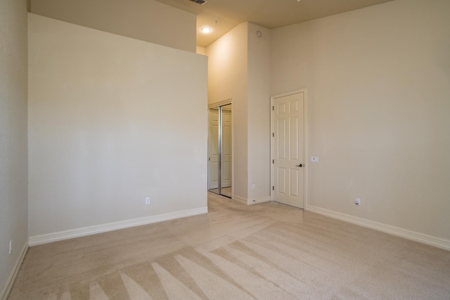 empty room featuring visible vents, baseboards, light colored carpet, and a high ceiling