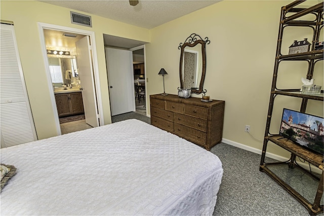 bedroom featuring ensuite bath, a textured ceiling, and dark colored carpet