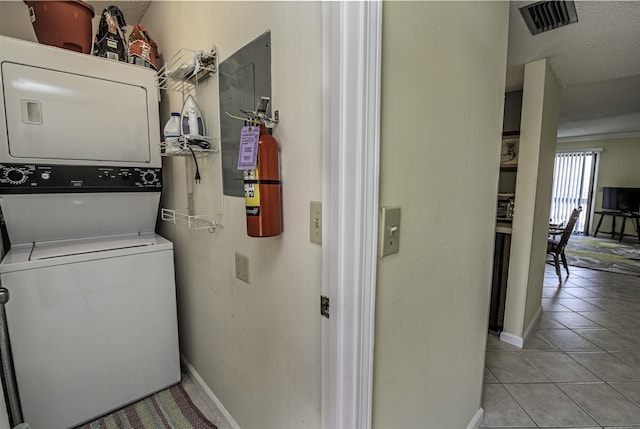 laundry area with light tile patterned flooring, a textured ceiling, and stacked washing maching and dryer