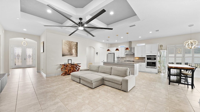 tiled living room with french doors, ceiling fan with notable chandelier, and a raised ceiling