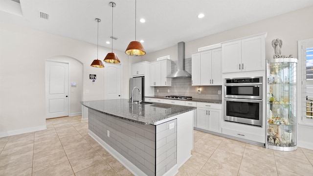 kitchen with white cabinets, pendant lighting, wall chimney range hood, and a kitchen island with sink