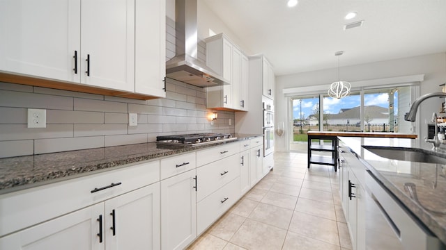 kitchen with sink, wall chimney range hood, dark stone counters, white cabinets, and appliances with stainless steel finishes