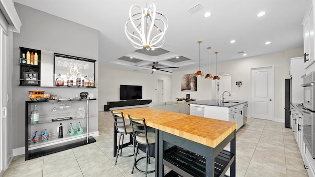 kitchen featuring ceiling fan with notable chandelier, a raised ceiling, sink, white cabinetry, and an island with sink