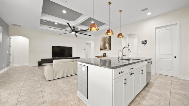 kitchen featuring sink, dark stone countertops, pendant lighting, a center island with sink, and white cabinets